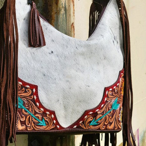 Cowhide leather bag with fringe and intricate designs, featuring 'The Rooster Den Co' branding.